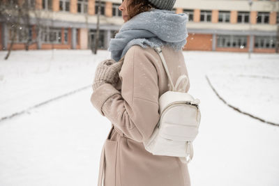A girl holds a white backpack with mittens in winter under the snow person