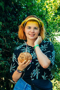 Portrait of smiling woman with coconut water standing against trees