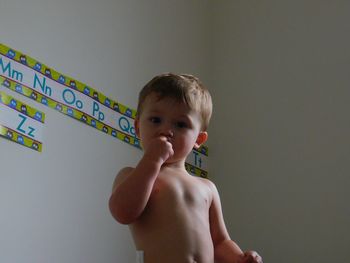 Portrait of shirtless boy standing against wall at home