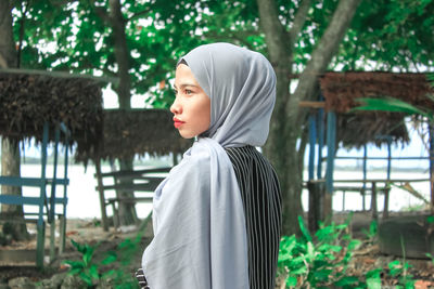 Portrait of beautiful young woman standing against trees