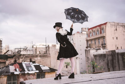 Rear view of woman holding umbrella while standing on terrace