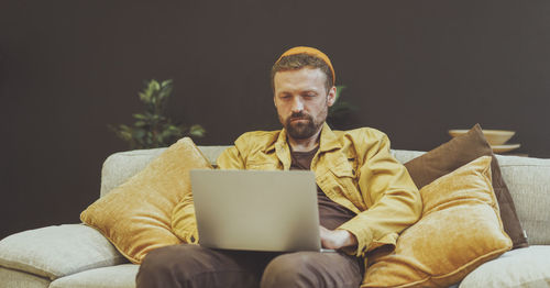 Young man using laptop while sitting on sofa at home