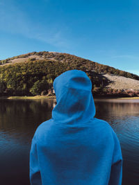 Rear view of man looking at lake against blue sky