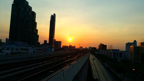 Railroad tracks amidst buildings in city against sky during sunset