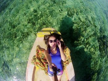 Directly above shot of young woman holding monopod while lying on boat during sunny day