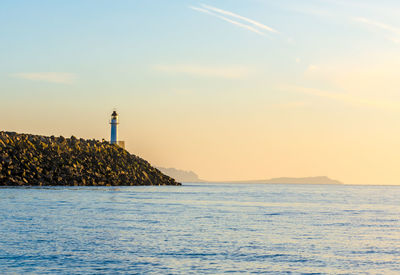 Lighthouse at sea shore against sky during sunset