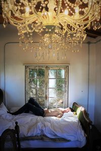 Portrait of shirtless teenage boy lying on bed by window at home