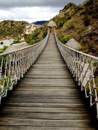 Footbridge leading towards mountain against sky