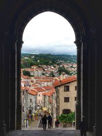 People walking by buildings in city against sky
