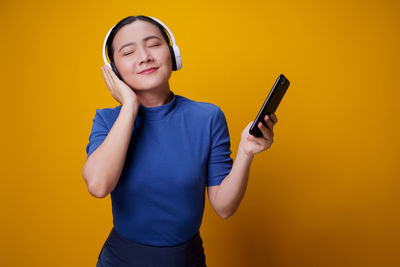 Full length of young man using smart phone against yellow background