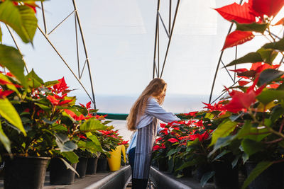 Side view of woman examining plants in greenhouse