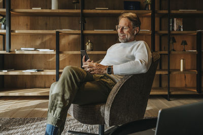 Smiling mature man using mobile phone while sitting on armchair