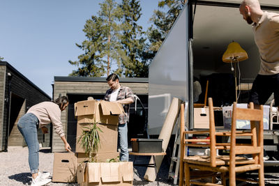 Couple opening cardboard boxes while delivery man unloading furniture from truck