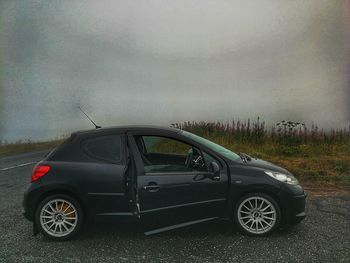 Car on road by field against sky