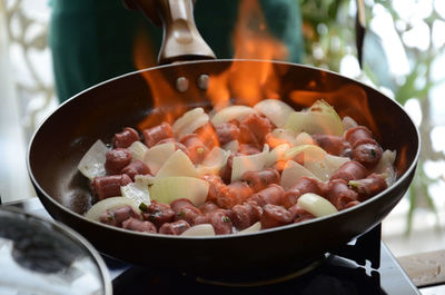 Close-up of flaming sausage and onions in frying pan