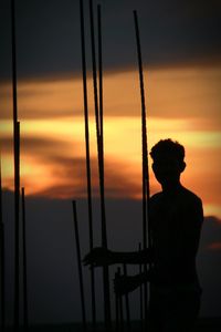 Silhouette man standing by iron rods against sky during sunset