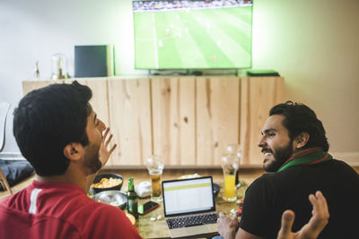 Male friends talking while watching soccer in living room