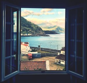 Buildings by sea against sky seen through window