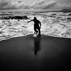 Silhouette man playing football at shore