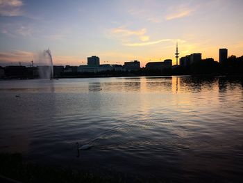 Scenic view of river by buildings against sky during sunset