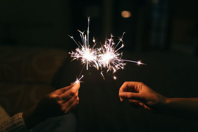 Cropped image of hands holding sparklers at night