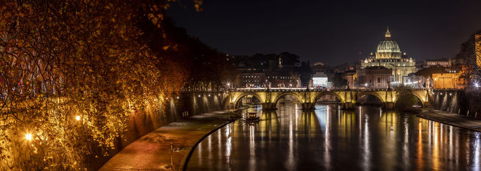 Illuminated bridge over river against buildings at night