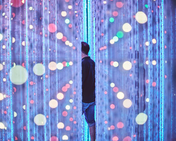 Rear view of man standing against illuminated lights at night