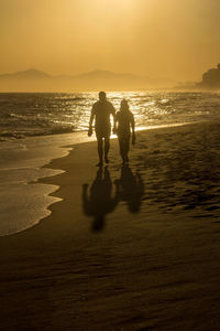 Silhouette people on beach against sky during sunset