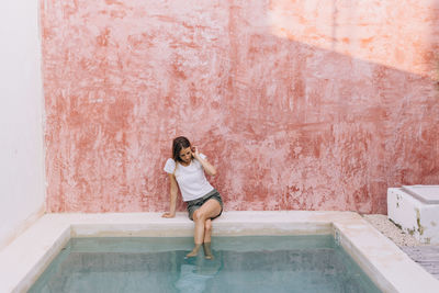 White woman sitting on the pool side with the feet on the water