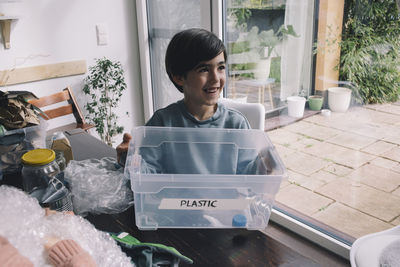 Smiling boy holding plastic container at home