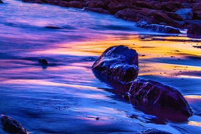 Close-up of rocks in sea against sky at sunset