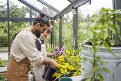 Side view of young man using mobile phone while standing in greenhouse