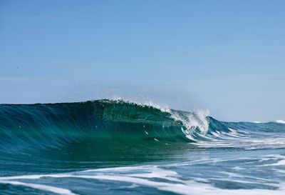 Wave splashing in sea against blue sky