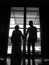 Full length of couple holding hands while standing against door at home