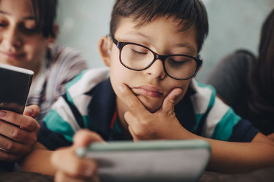 Close-up of disabled boy with closed eyes holding digital tablet while lying with sisters on bed at home