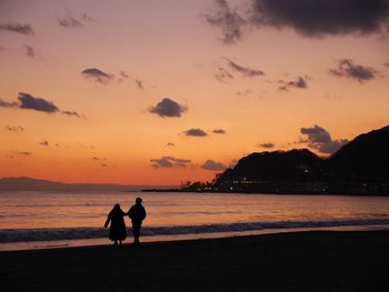 Silhouette friends on beach against sky during sunset