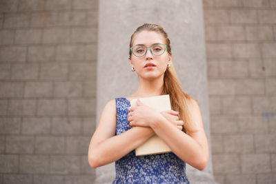 Portrait of young woman standing against wall