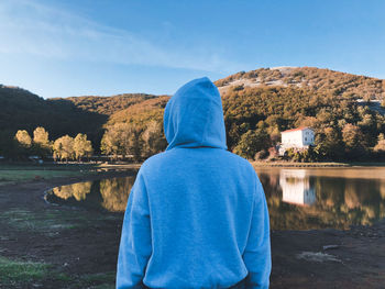 Rear view of woman wearing hood looking at lake against sky