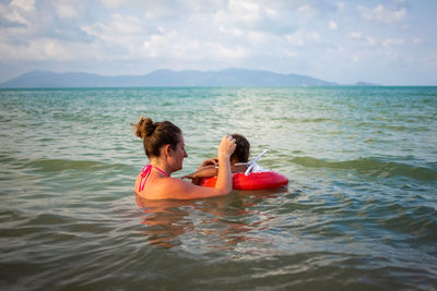 Mother with daughter enjoying in sea against sky