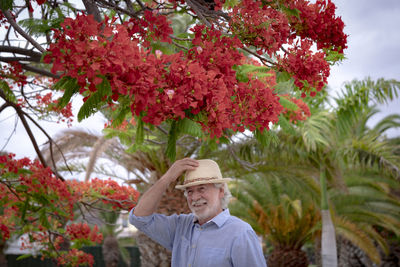 Smiling senior man wearing hat standing against flowering tree outdoors