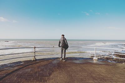 Rear view of man standing at promenade against blue sky