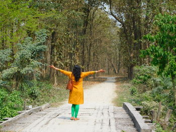 Rear view of woman walking on footpath amidst trees in forest