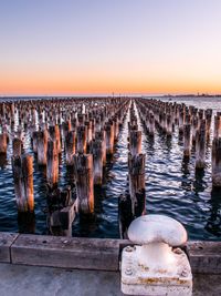 Wooden posts in sea against sky during sunset