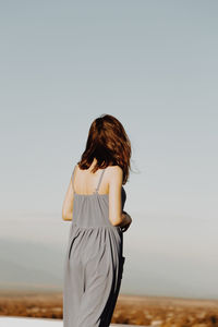 Rear view of young woman standing against clear sky