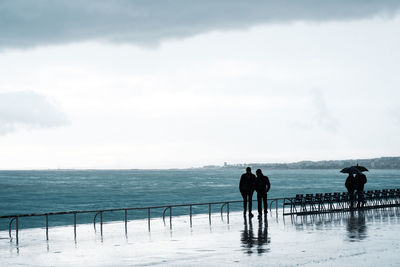 Silhouette people standing at beach against sky