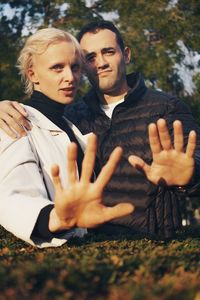 Portrait of couple gesturing while standing in park against trees