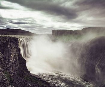 Scenic view of waterfall against cloudy sky