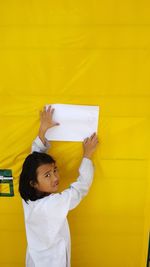 Portrait of girl sticking paper on yellow wall