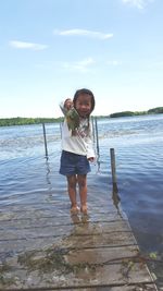 Portrait of smiling girl holding fish while standing at lake against sky
