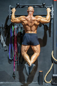 Shirtless bodybuilder practicing chin-ups in gym